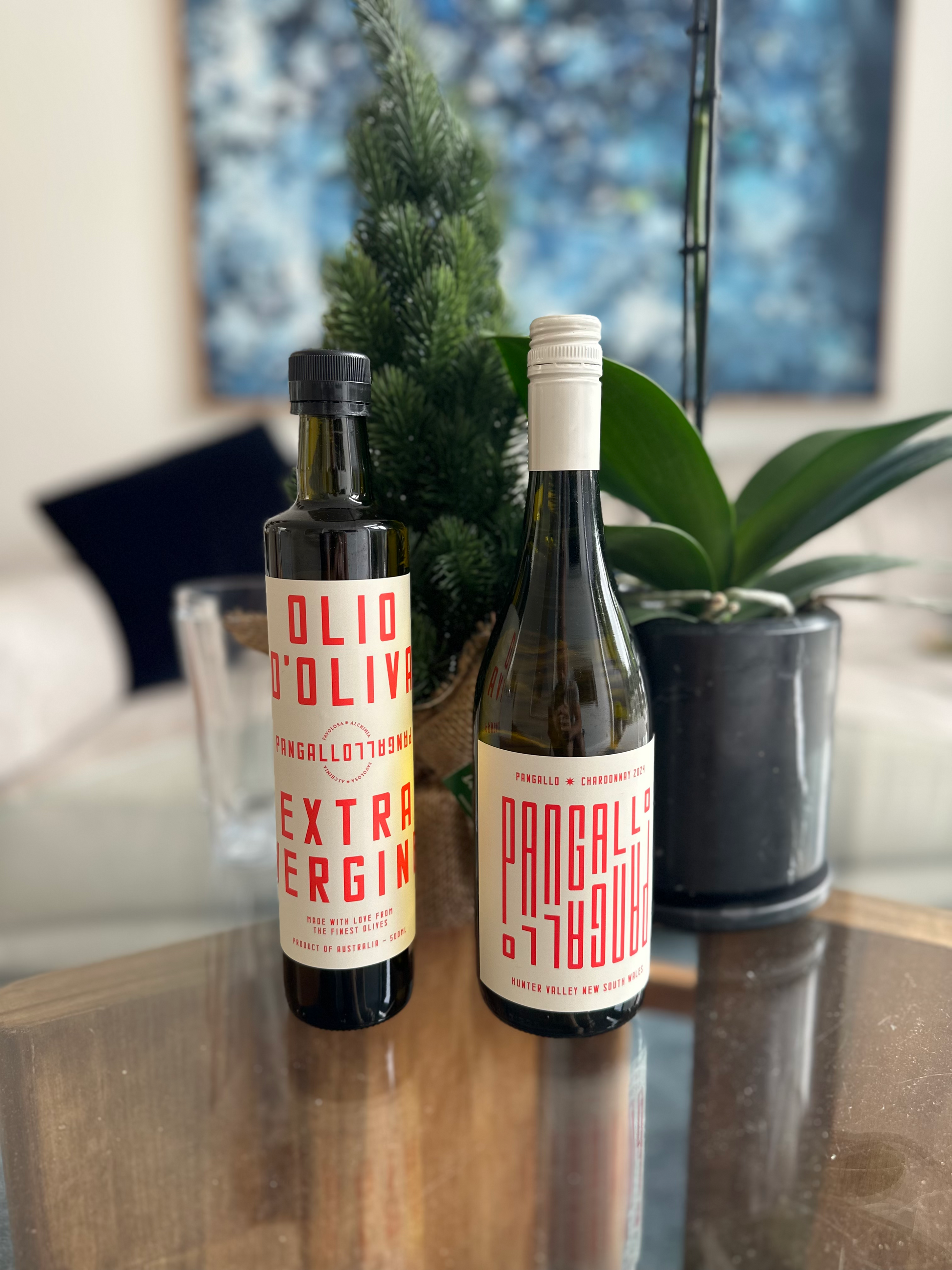 A bottle of olive oil and chardonnay on a glass table with a blurred indoor background